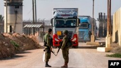 Soldados israelíes hacen guardia mientras camiones con ayuda humanitaria se aproximan. Toma captada en el lado israelí del cruce fronterizo de Kerem Shalom con el sur de la Franja de Gaza el 19 de diciembre de 2023.