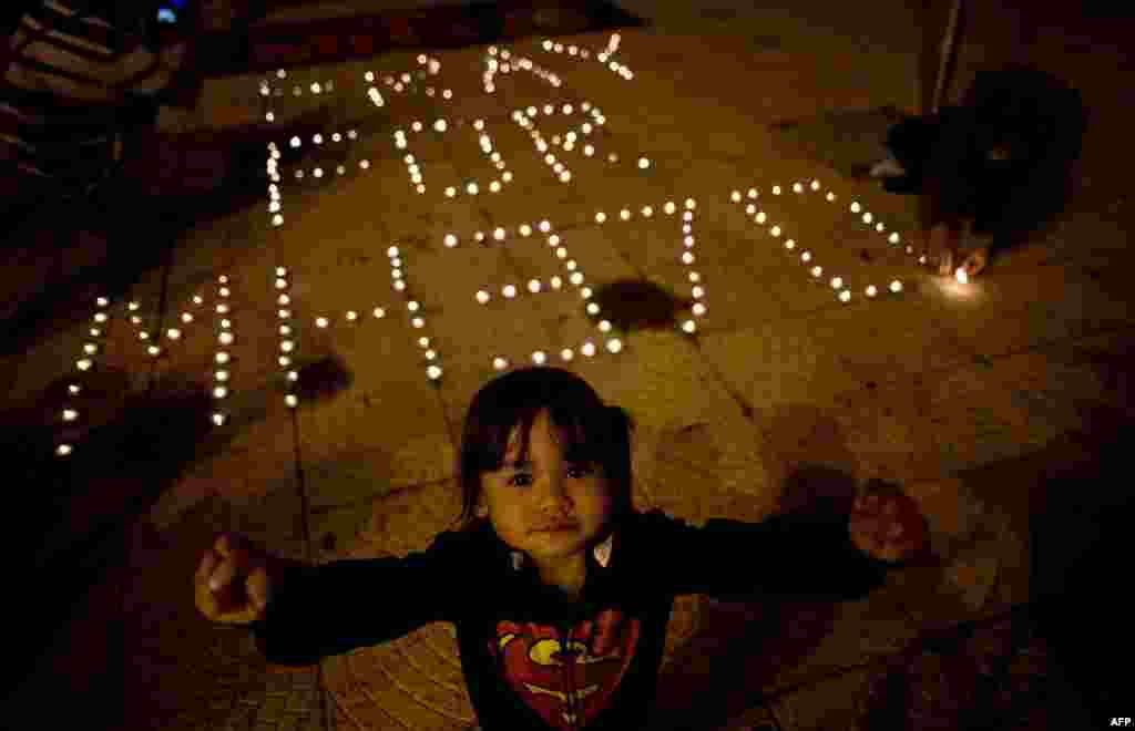 A child reacts to the camera as others light candles during a vigil for missing Malaysia Airlines passengers at the Independence Square in Kuala Lumpur, March 10, 2014.