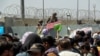 Un soldado estadouniense sostiene un letrero que indica que una puerta está cerrada mientras cientos de personas reúnen algunos documentos, cercaa de un puesto de control de evacuación en el aeropuerto de Kabul el 26 de agosto de 2021.