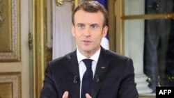 Seorang pria dengan tulisan “Macron mundur” mengibarkan bendera Perancis, semetara pengunjuk rasa “rompi kuning” berkumpul untuk memprotes kenaikan harga bahan bakar minyak dan biaya hidup di jalan tol La Barque, dekat Marseille, selatan Perancis, 9 Desember 2018.