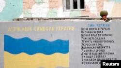 俄罗斯军人在克里米亚国际机场的一堵墙后面站岗，墙上画着乌克兰国旗，写着乌克兰国歌歌词