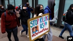 A protester holding a sign reading "Stop Killing Us" navigates along Chicago's Loop during a peaceful protest, Wednesday, April 14, 2021, ahead of the video release of the fatal police shooting of 13-year-old Adam Toledo. (AP Photo/Shafkat Anowar)