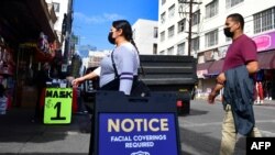 Un letrero recuerda a las personas el requisito de cubrirse la cara ya que los peatones usan mascarillas debido al coronavirus en Los Ángeles, California, el 12 de noviembre de 2020. - (Foto de Frederic J. BROWN / AFP)