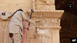 FILE - This image from a video posted on a website frequently used by Islamic State shows a militant hammering at a face on a wall in Iraq's ancient city of Hatra, April 3, 2015.