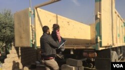 A father loads his child into an army truck to go to an internally displaced persons' camp in the Mosul suburbs, Iraq, Nov. 12, 2016. (H.Murdock/VOA)
