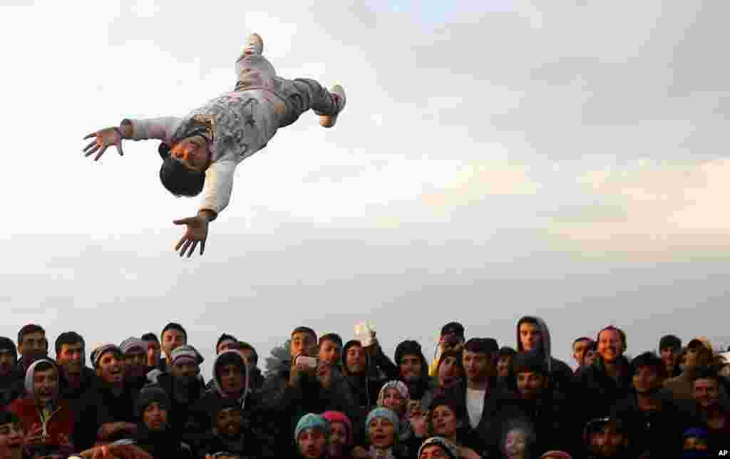 A person is thrown and caught as migrants gather and have a party in the northern Greek border station of Idomeni. 