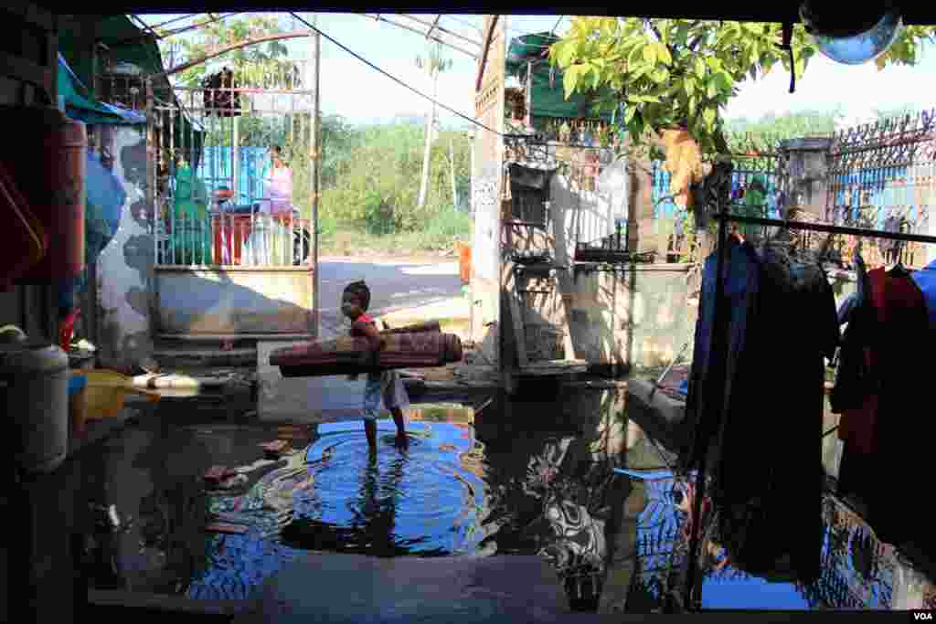 A girl stands in flood water, holding a sleeping mat in front of Khoeun Sovat’s house in Boeung Kak community in Phnom Penh, Cambodia, Nov. 13, 2014. (Nov Povleakhena/VOA Khmer)