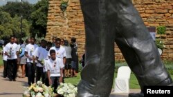 Para siswa meletakkan karangan bunga di bawah patung Nelson Mandela di Johannesburg memperingati setahun wafatnya mendiang pemimpin anti apartheid itu.
