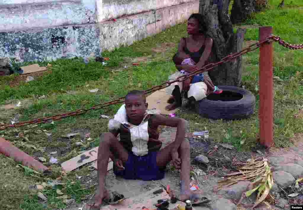 Assis devant une femme sans arbi portant un bébé, un enfant abandonné dans la rue répare ses chaussures de fortunes sur la bordure d'une rue de Kinshasa, capitale de la République Démocratique du Congo, juin 2013. (Reuters)