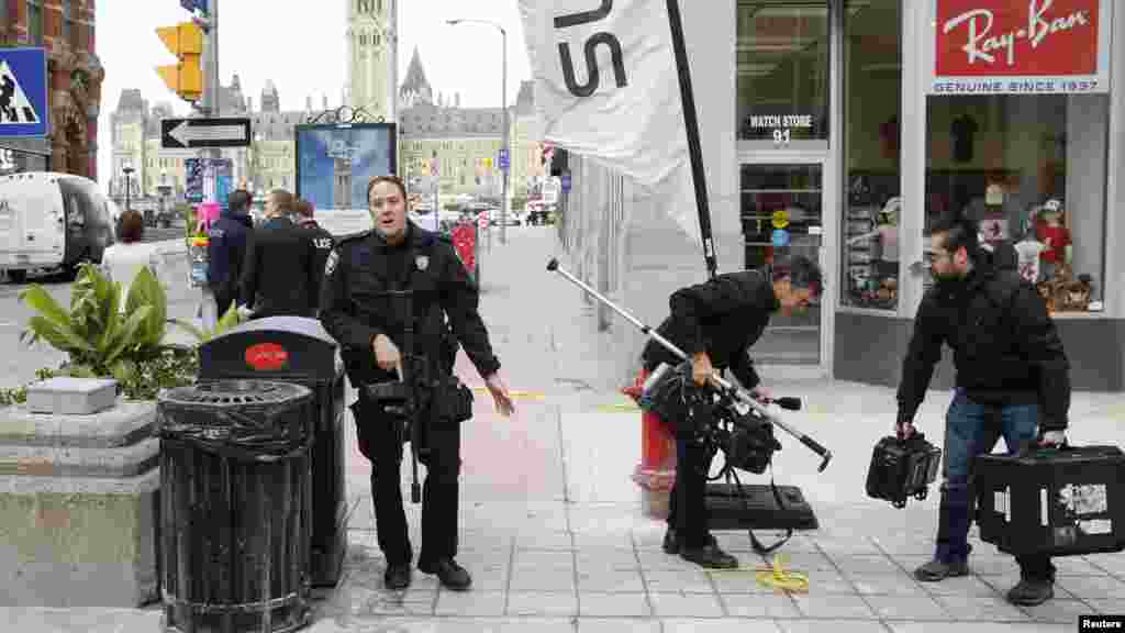 Un officier de police d'Ottawa en train de disperser des journalistes près du lieu de la fusillade, sur la rue Metcalfe après une attaque meurtrière à Ottawa, le 22 octobre 2014.