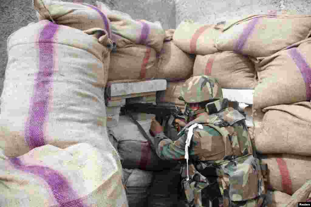 A Syrian Army soldier loyal to Syria's President Bashar al-Assad takes a position behind sandbags as he points his weapon in Ard al-Hamra, Aleppo, Feb. 27, 2014. 