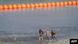 Migrantes caminan entre alambre de concertina y una serie de boyas colocadas en el agua a lo largo de la frontera de Río Grande con México para evitar la entrada de inmigrantes ilegales a EEUU en Eagle Pass, EEUU, el 16 de julio de 2023.