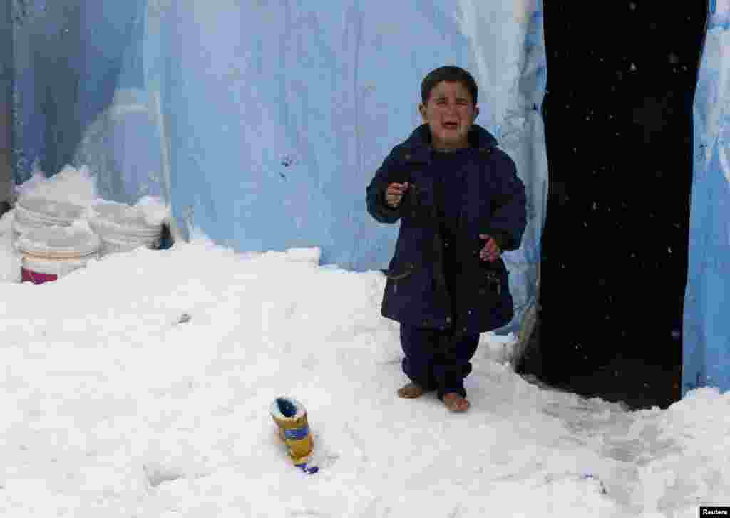 Seorang anak pengungsi Suriah menangis saat berdiri tanpa sepatu di atas salju yang turun di kamp pengungsi Zahle, di Lembah Bekaa, Lebanon. 