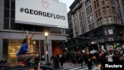 Personas gritan desde un vehículo, en Boston, Massachusetss, mientras otros marchan bajo un rótulo con el nombre de George Floyd, quien murió bajo custodia de la policía de Minneapolis. 