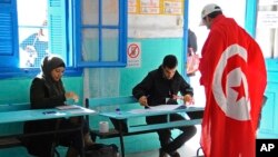 Un Tunisien drapé au drapeau national arrive à un bureau de vote pour voter à La Marsa, dans la banlieue de Tunis, en Tunisie, le 21 décembre 2014.