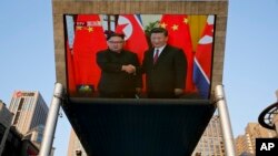 Orang-orang bersepeda melewati layar TV raksasa yang menyiarkan pertemuan pemimpin Korea Utara Kim Jong Un dan Presiden Xi Jinping dalam upacara penyambutan di Aula Besar Rakyat di Beijing, 19 Juni 2018.
