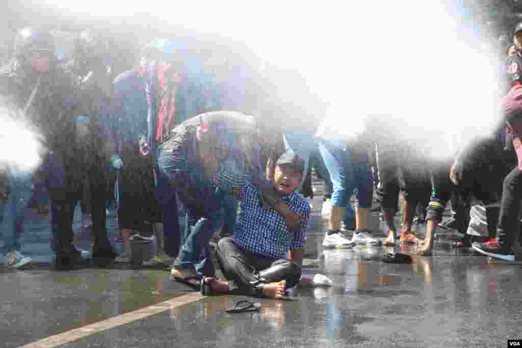 A protester is helped by a fellow protester at a rally against Myanmar's military coup in Mandalay as riot police use water cannons to disperse demonstrators, Feb. 9, 2021. (Credit: VOA Burmese Service)
