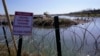 Migrantes cruzan el río Bravo a EEUU desde México detrás de un hilo de cuchillas y un cartel que advierte que cruzar es peligroso e ilegal, el miércoles 3 de enero de 2024 en Eagle Pass, Texas. 