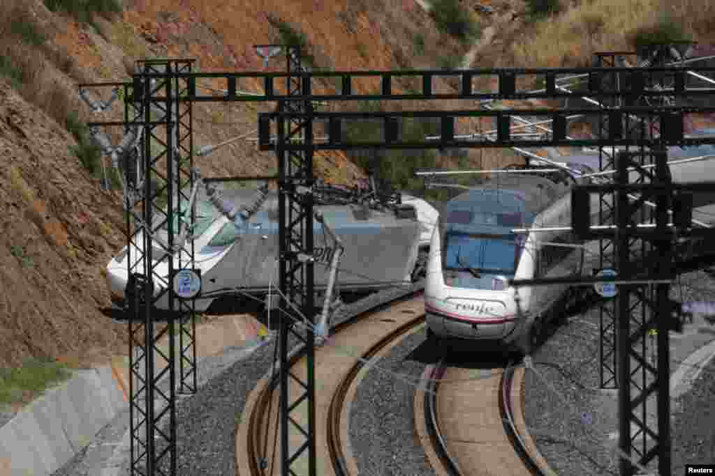 A passenger train passes by a wrecked train engine at the site of the train crash in Santiago de Compostela, northwestern Spain, July 26, 2013. 