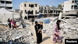 ARCHIVO - Una mujer palestina lleva a un niño mientras caminan entre los escombros de las casas destruidas en ataques anteriores durante la ofensiva militar israelí, en Khan Younis, en el sur de la Franja de Gaza, el 6 de noviembre de 2024