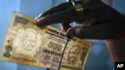 An employee checks a 500 Indian rupee note at a cash counter inside a bank in the northeastern Indian city of Agartala, August 9, 2011.
