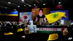 Los partidarios de Hizbulá levantan sus puños a modo de saludo mientras escuchan un discurso del líder, Sayyed Hassan Nasrallah, a través de un enlace de video, en una ceremonia que marca el "Día del Mártir de Hezbollah", en el sur de Beirut, Líbano. Sábado, 11 de noviembre.