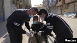 شام کے شہر قامشلی میں لاک ڈاؤن کے دوران ریسکو ورکر ایک شخص کو وہیلز چیئر پر اسپتال لے جا رہے ہیں۔ 23 مارچ 2020