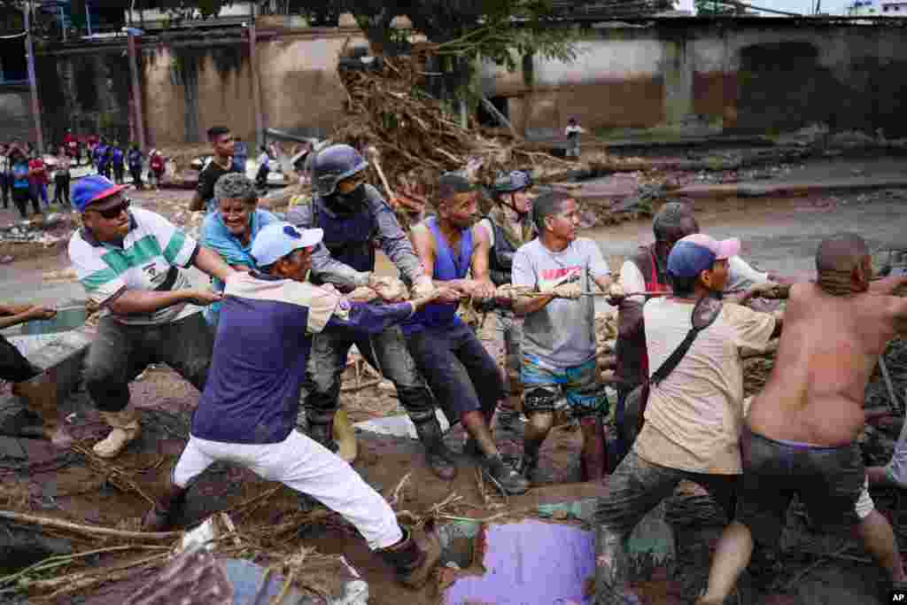 Los residentes locales y los trabajadores de socorro tiran de una cuerda para retirar los escombros en busca de sobrevivientes de una casa destruida por las inundaciones.