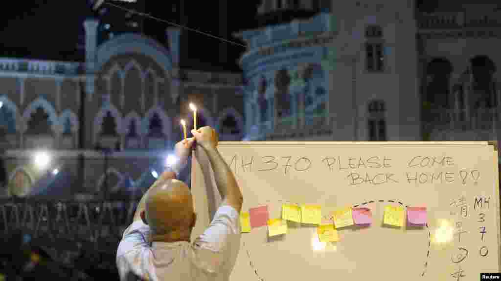 A man places a candle on top of a white board set up to place messages for passengers on Flight MH370 during a candlelight vigil in Kuala Lumpur, April 6, 2014.