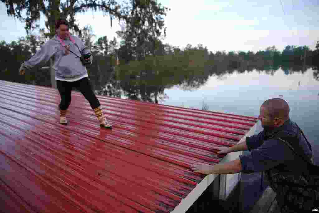 Wendy Lawshe (L) walks along the roof of her father's house as her husband waits for her in a boat as they retrieve pictures from the walls of the home that is flooded in in Andrews, South Carolina. The state has experienced record rainfall amounts causing severe flooding and officials expect the damage from the flooding waters to be in the billions of dollars.