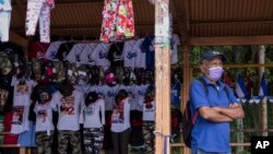 Un hombre espera un autobús de transporte público junto a un puesto que vende camisetas, banderas y gorras, con un tema sandinista, en una parada de autobús en Managua, Nicaragua, el miércoles 3 de noviembre de 2021. Foto AP/Andrés Núñez
