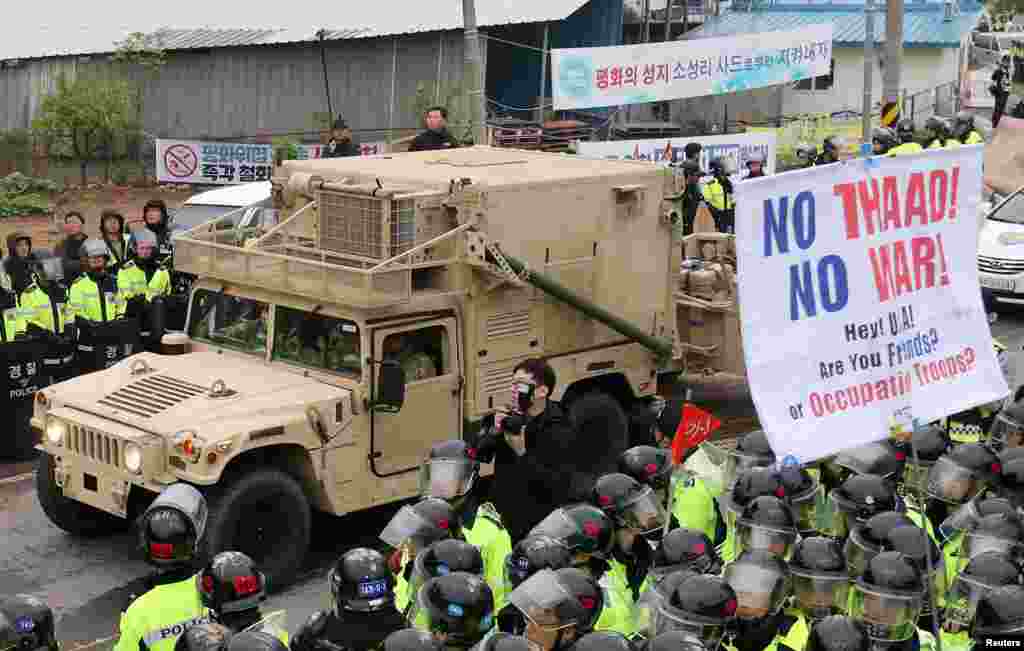 美国驻韩国部队提供的图片显示,卡车运送萨德系统的导弹发射器和其他设备,抵达美国在韩国的空军基地。在军人的后面有韩国示威者,举着标语“不要萨德!不要战争!”(2017年3月6日)。