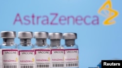 Des flacons étiquetés «Vaccin contre le coronavirus Astra Zeneca COVID-19» et une seringue sont visibles devant un logo AstraZeneca affiché, sur cette photo d'illustration prise le 14 mars 2021.