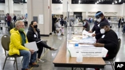Petugas pemilihan (kanan) memverifikasi surat suara diawasi oleh para pengamat penghitungan ulang (kiri) dalam penghitungan surat suara pilpres secara manual di the Wisconsin Center, 20 November 2020. (Foto: AP)