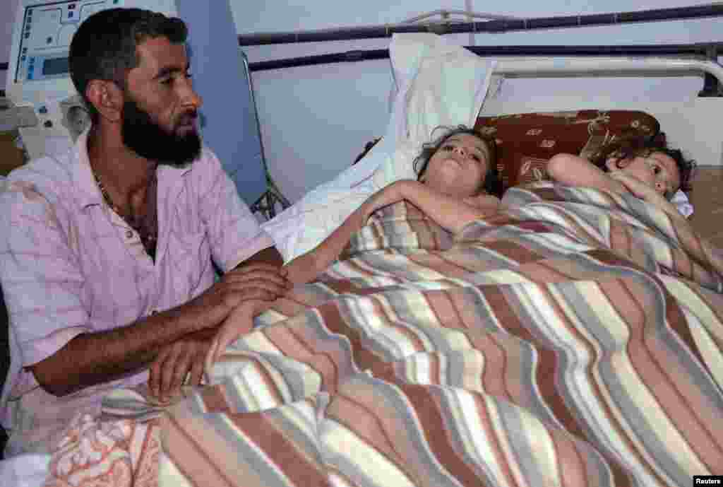 A man sits in a hospital near two children who activists say were affected by toxic gas near Damascus, August 21, 2013.