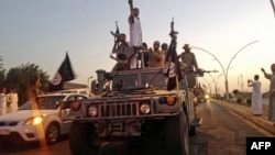 FILE - Fighters from the Islamic State group parade in a commandeered Iraqi security forces vehicle in Mosul, Iraq.
