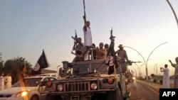 FILE - Fighters from the Islamic State group parade in a commandeered Iraqi security forces vehicle in Mosul, Iraq.