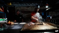 ARCHIVO - Un vendedor ambulante prepara comida iluminado por una bombilla alimentada por un generador en medio de apagones en Manta, Ecuador, el lunes 23 de septiembre de 2024.