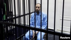 FILE - Saadi Gadhafi, son of Moammar Gadhafi, sits behind bars during a hearing at a courtroom in Tripoli, Libya, Feb. 7, 2016.