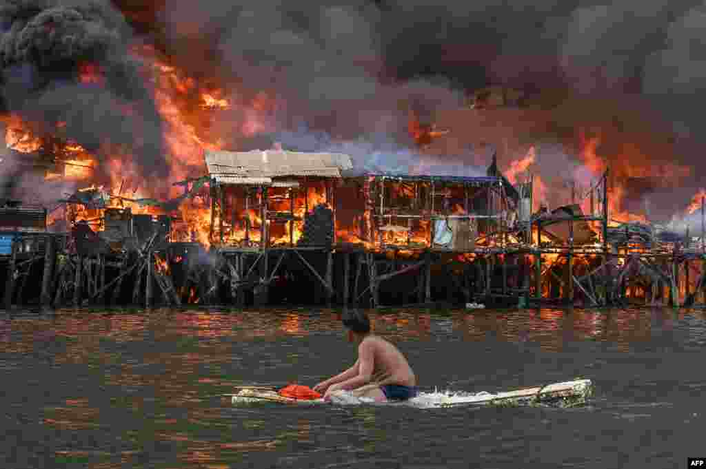 A man watches houses on fire at Tondo in Manila, Philippines. Raging orange flames and thick black smoke billowed into the sky, as fire ripped through hundreds of houses in a closely built slum area of the capital.