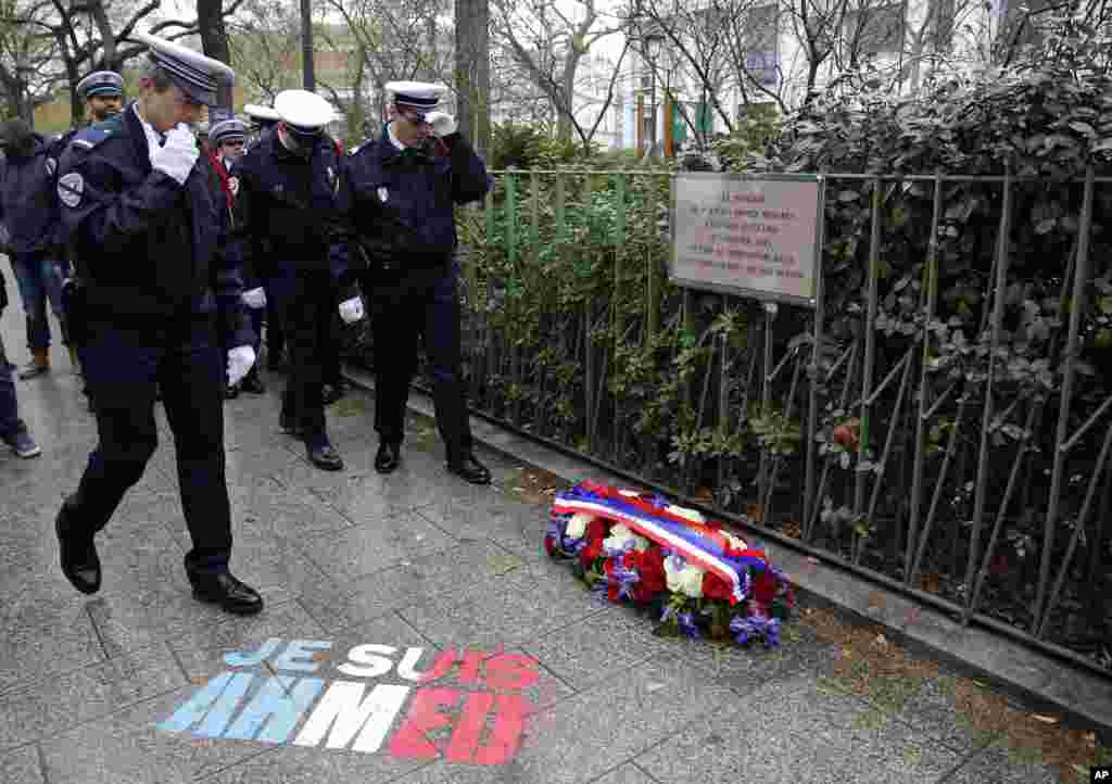 Policemen walk past spray painted on the sidewalk reading: "Je suis Ahmed," or "I am Ahmed," in the red, white and blue of the French flag near a plaque commemorating late police officer Ahmed Merabet in Paris, France. President Francois Hollande honored 17 victims killed in Islamic extremist attacks on satirical newspaper Charlie Hebdo, a kosher market and police a year ago this week.