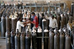Personas cargan cilindros de oxígeno después de rellenarlos en una fábrica, en medio de la propagación de la enfermedad del coronavirus (COVID-19) en Ahmedabad, India, el 25 de abril de 2021.