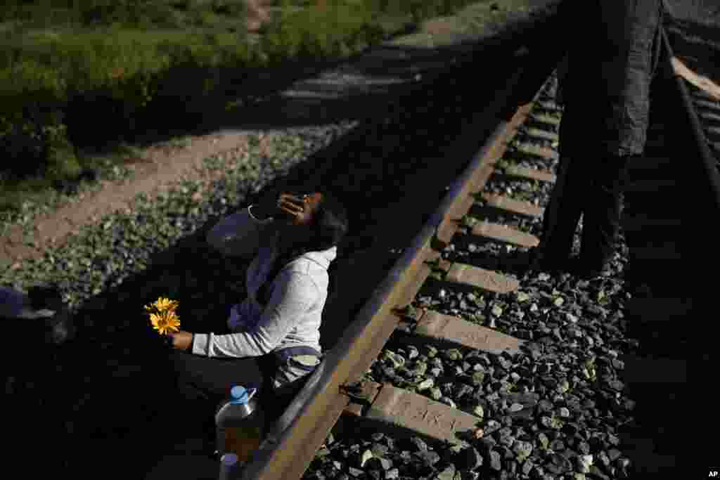 En la dura travesía una migrante venezolana se ríe mientras aprovecha para bromear con su esposo, quien le regaló algunas flores que recogió en el pasto, en un momento en que esperan a lo largo de las vías del tren con la esperanza de abordar un tren de carga hacia el norte en Huehuetoca, México, el 20 de septiembre. 2023. [Foto: Eduardo Verdugo]