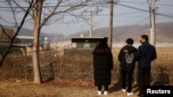 资料照:2021年2月12日,在韩国农历新年到来之际,一名脱北者和他的孩子们站在京畿道坡州市非军事区附近的铁丝网前。(路透社)