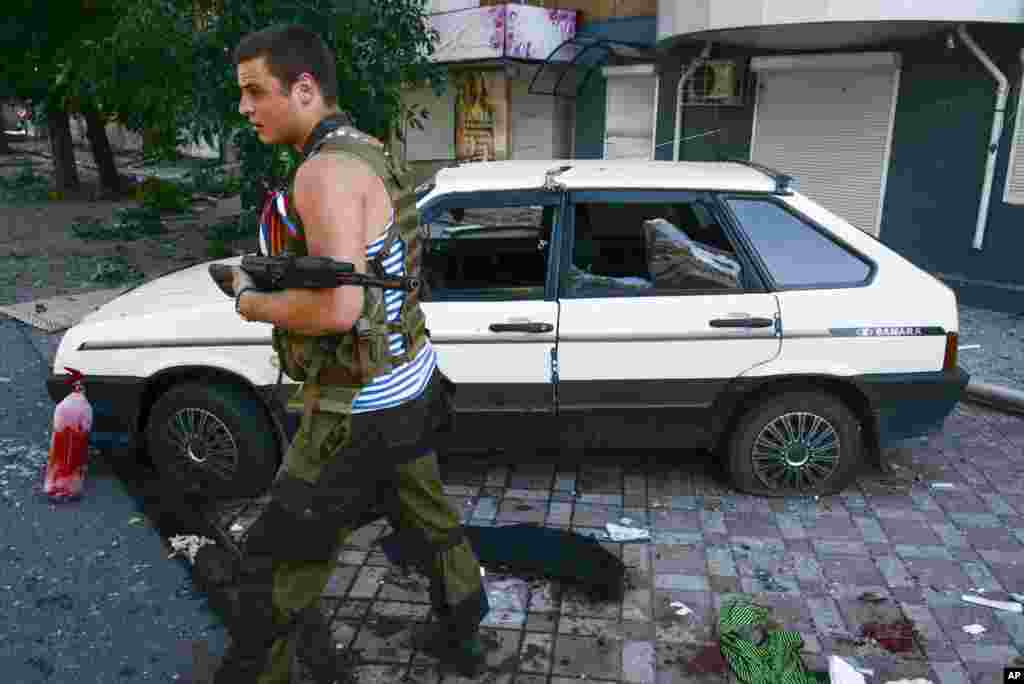 A Pro-Russian rebel passes by a car which was hit by shrapnel from a shell in the town of Donetsk, eastern Ukraine, Aug. 27, 2014. 