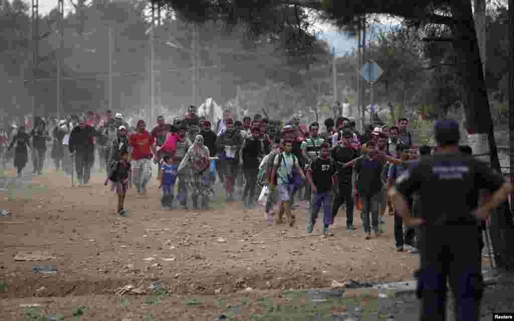 Migrants walk towards the border line crossing the Macedonian-Greek border as a Greek policeman watches near Gevgelija, Macedonia, Sept. 6, 2015.