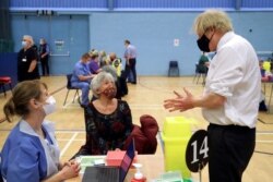 Britain's Prime Minister Boris Johnson speaks with a woman waiting to receive an Oxford-AstraZeneca COVID-19 vaccine, during his visit at a vaccination center at Cwmbran Stadium in Cwmbran, south Wales, Britain, Feb. 17, 2021.