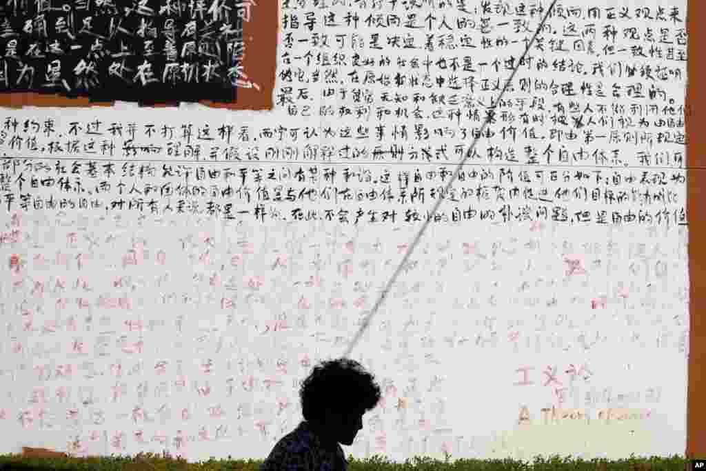 Seorang wanita berjalan melewati dinding ditutupi dengan karakter Cina dari sebuah bab dari buku John Rawls '"A Theory of Justice" di luar sebuah galeri seni di Beijing.