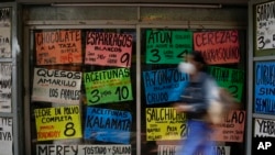 Una mujer camina frente a carteles que muestran los precios de los productos en dólares, frente a una tienda en Caracas, el 18 de enero de 2022. Foto: AP.