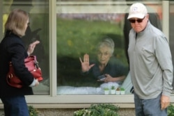 Judie Shape, center, who has tested positive for the coronavirus, but isn't showing symptoms, presses her hand against her window after a visit through the window and on the phone with her relatives, March 17, 2020, in Kirkland near Seattle.